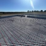 Wide agricultural landscape showing completed outdoor radiant heating system with white concrete basin and piping grid