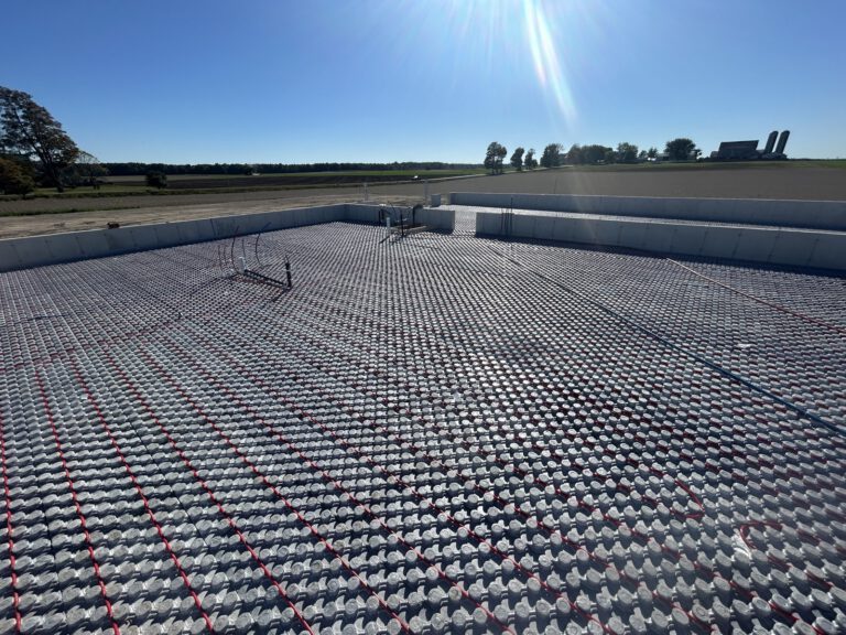 Wide agricultural landscape showing completed outdoor radiant heating system with white concrete basin and piping grid