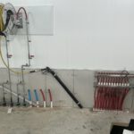Radiant floor heating manifold detail showing wire reels, color-coded pipe connections, and valve assembly