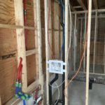 House framing under construction with red and blue PEX tubing installed for radiant floor heating