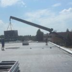 Crane lifting rooftop HVAC unit onto building