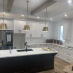 Modern kitchen with white cabinetry, black island, stainless steel appliances, brass pendants
