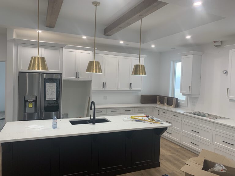 Modern kitchen with white cabinetry, black island, stainless steel appliances, brass pendants