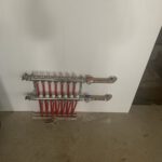 Radiant heating manifold with red tubing on white drywall