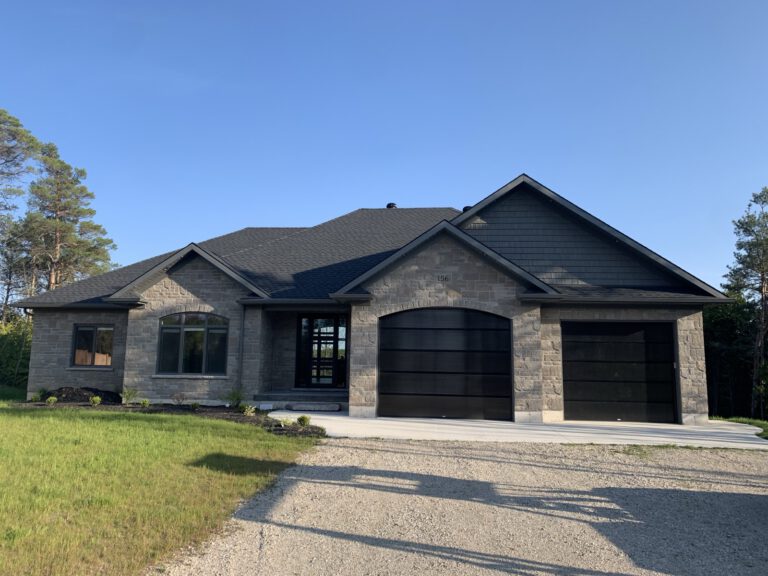 Modern stone home with dark roof, black garage doors, and mature landscaping