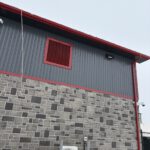Corner exterior detail with red metal panel, stone facade, and HVAC unit