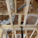 Interior framing with blue hydronic piping and wrapped insulation batts