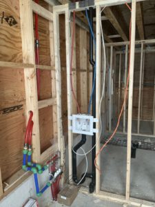 House framing under construction with red and blue PEX tubing installed for radiant floor heating