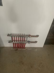 Radiant heating manifold with red tubing on white drywall
