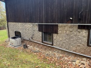 Generator installation showing mounted unit with gas piping against stone foundation