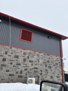 Corner exterior detail with red metal panel, stone facade, and HVAC unit