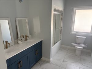 Finished bathroom with dual vanity, navy cabinets, marble tile