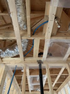 Interior framing with blue hydronic piping and wrapped insulation batts