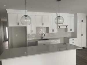 Modern kitchen with white cabinetry, gray quartz countertops, and pendant lights